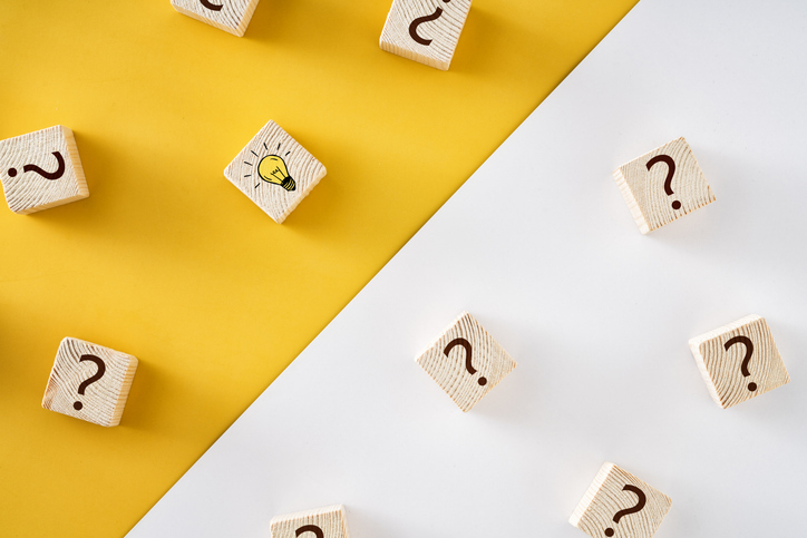 Wooden blocks with question marks and a single lightbulb block, illustrating the difference between lead generation and demand generation in B2B marketing.